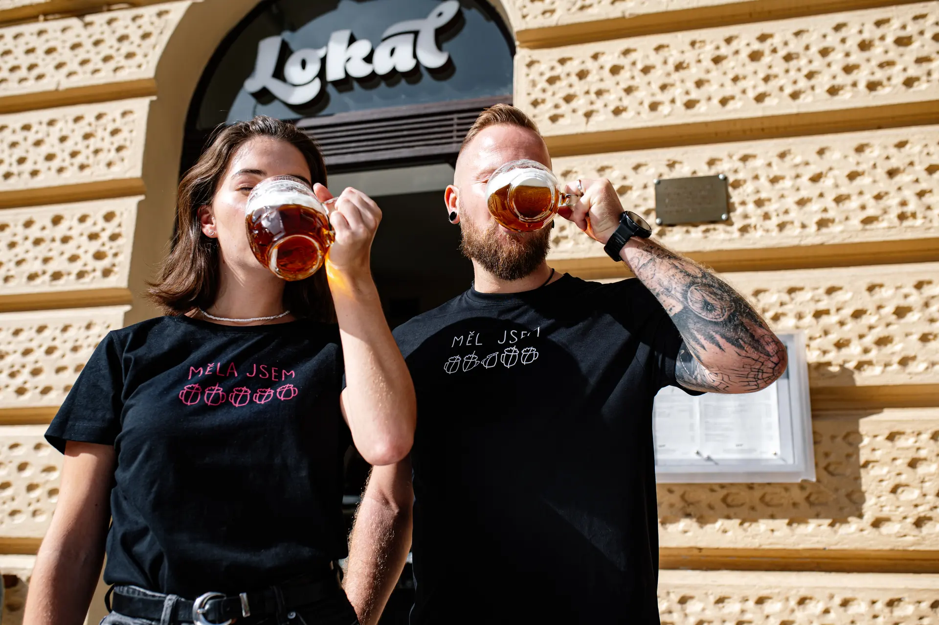 Dva lidé pijí čepované pivo před restaurací Lokál.
