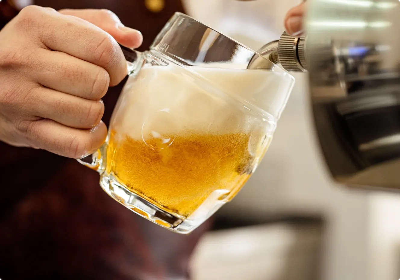 Pouring beer into a glass mug with a thick foam head.
