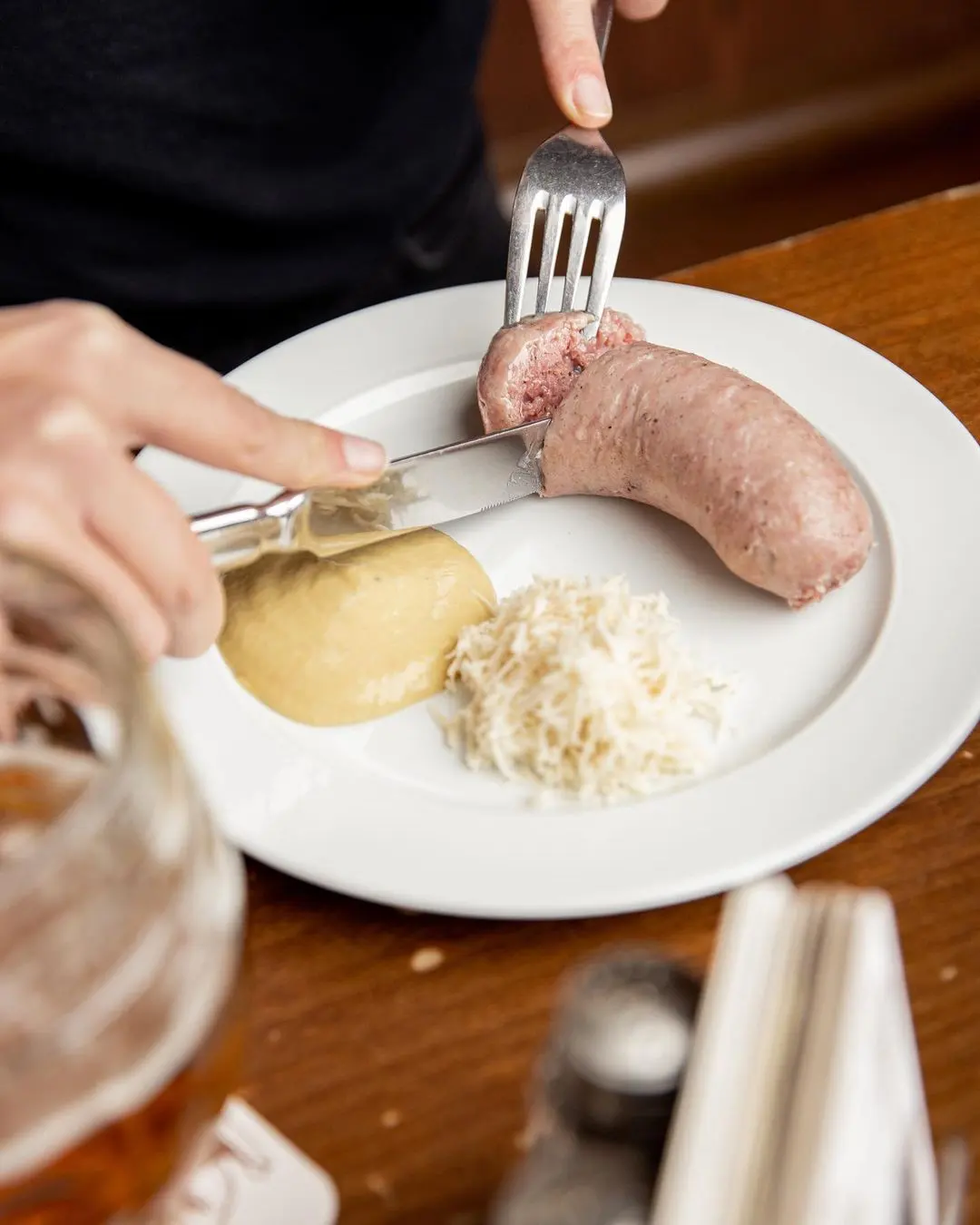Close-up of traditional Czech sausage served with horseradish and mustard on a white plate in a pub.