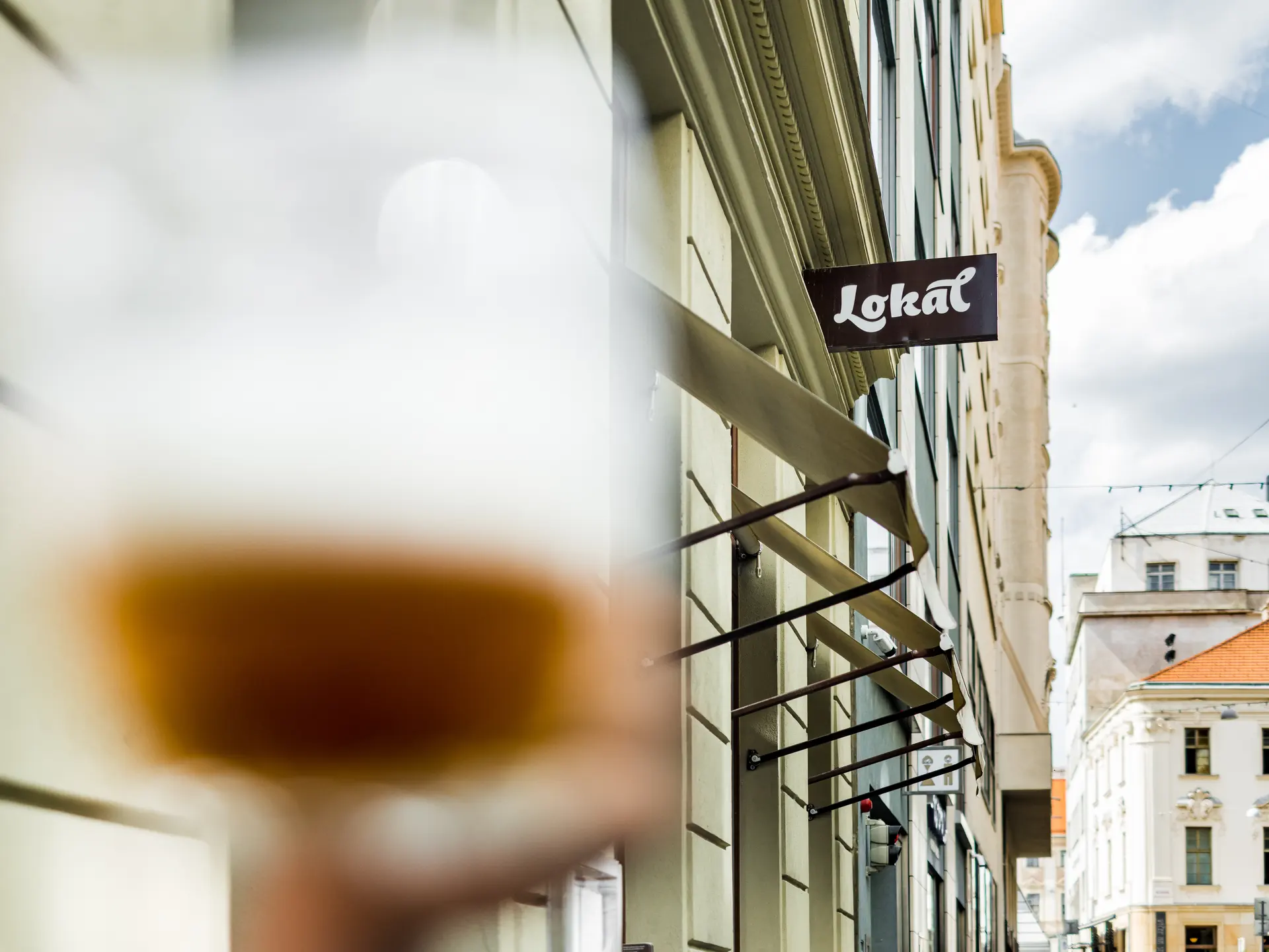 Exteriér restaurace Lokál U Caipla s vývěsním štítem Lokál a rozostřeným půllitrem piva v popředí.